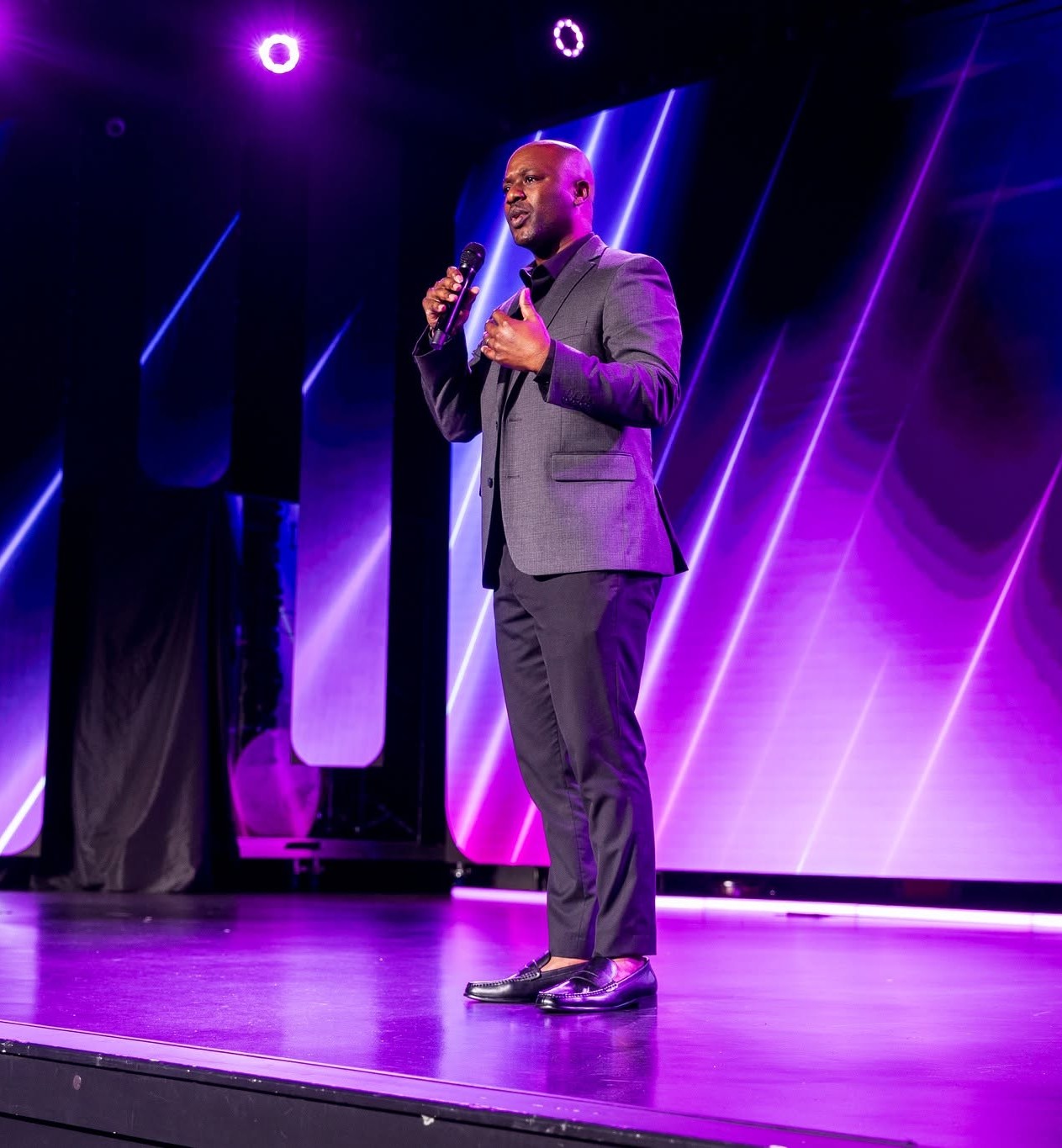 Neco Johnson on a purple-lit arena stage with a microphone